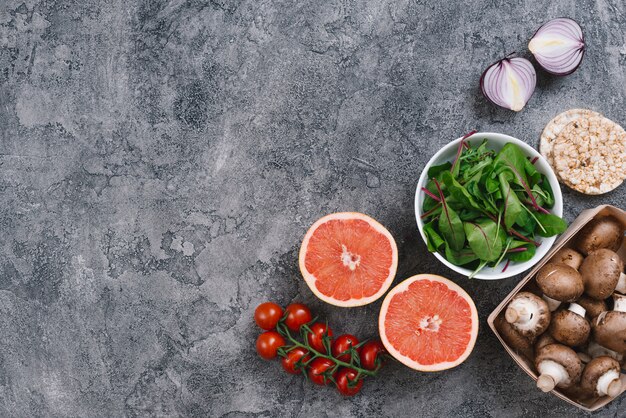 Foto gratuita una vista aérea de setas; rodaja de pomelo; cebolla; espinacas; tomates cherry y pastel de arroz inflado sobre fondo gris con textura