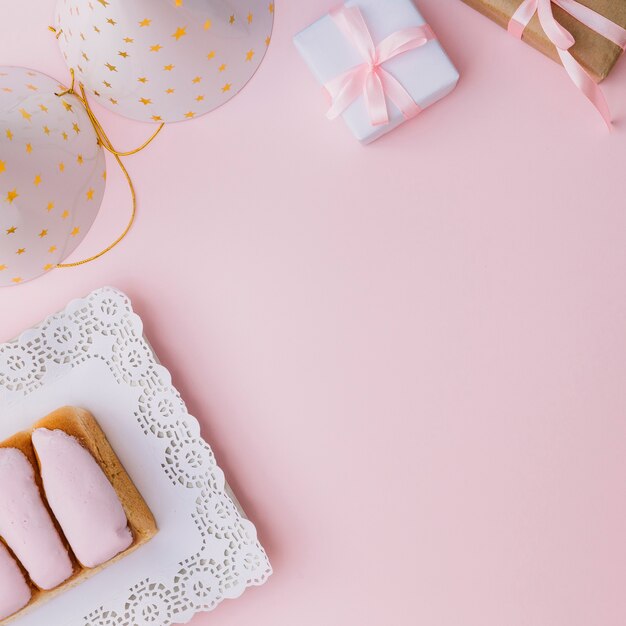 Una vista aérea del sombrero de fiesta; caja de regalo; y bollos helados sobre fondo rosa