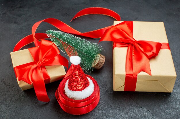 Vista aérea del sombrero de santa claus en un rollo de cinta y hermosos regalos árbol de navidad sobre fondo oscuro