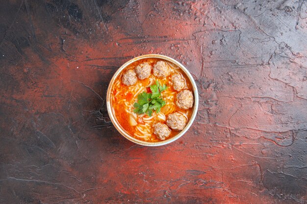 Vista aérea de sopa de albóndigas con fideos en un recipiente marrón sobre fondo oscuro