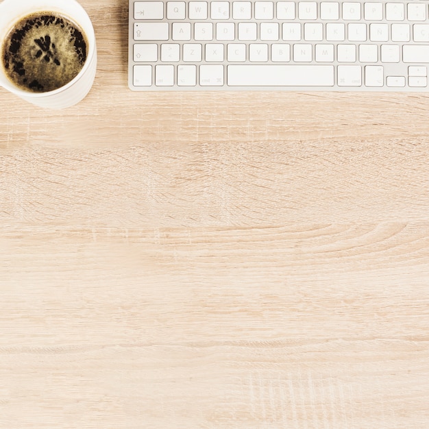 Una vista aérea de la taza de café y el teclado en la mesa de madera