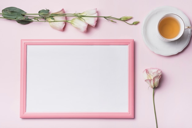 Una vista aérea de la taza de té con marco de fotos y flores de eustoma sobre fondo rosa