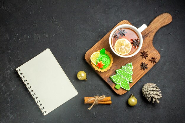 Vista aérea de una taza de té negro, accesorios navideños, cono de coníferas y cuaderno de limas canela