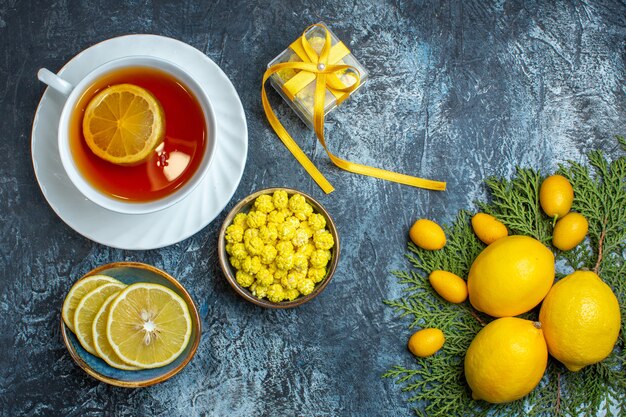 Vista aérea de una taza de té negro con caramelos de limón y caja de regalo la mitad de la colección entera de frutas cítricas en ramas de abeto sobre fondo oscuro