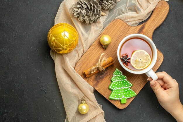 Vista aérea de una taza de té negro con limón y canela accesorios de decoración de año nuevo en la tabla de cortar de madera