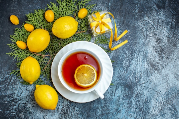 Vista aérea de una taza de té negro con limón y colección de cítricos frescos orgánicos naturales en ramas de abeto sobre fondo oscuro