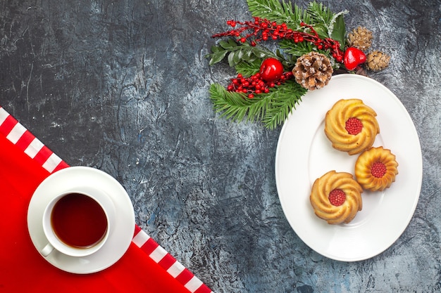 Vista aérea de una taza de té negro sobre una toalla roja y galletas en un plato blanco accesorios de año nuevo en superficie oscura