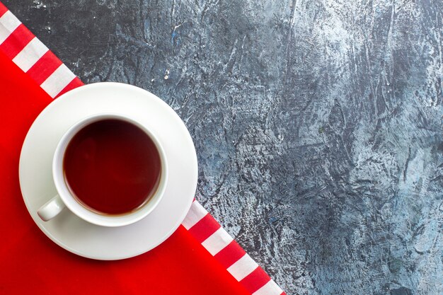 Vista aérea de una taza de té negro sobre una toalla roja en el lado derecho sobre una superficie oscura