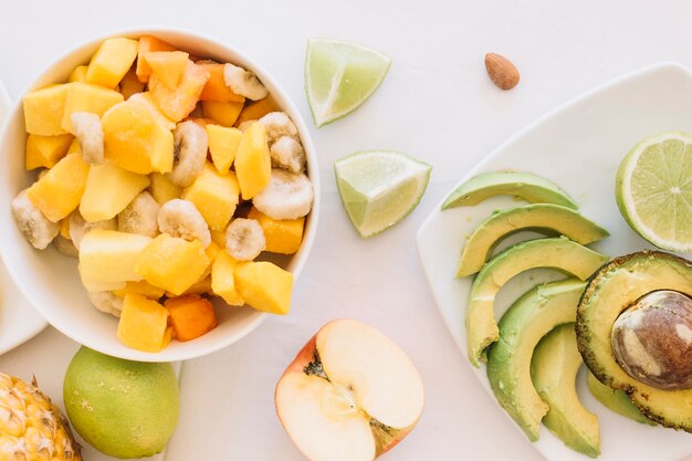 Una vista aérea del tazón de ensalada de frutas y las rebanadas de aguacate sobre fondo blanco