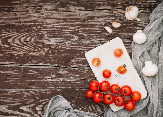 Una vista aérea de tomates cherry rojos; dientes de ajo y champiñones en mesa de madera