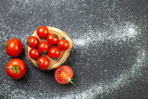 Vista aérea de tomates frescos con tallos en tablero de madera en el lado derecho sobre fondo negro blanco