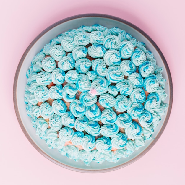 Una vista aérea de la torta decorada con crema batida azul en un plato contra un fondo rosado