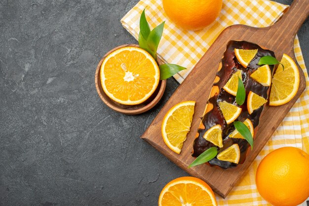 Vista aérea de tortas blandas enteras y naranjas cortadas con hojas en la mesa oscura