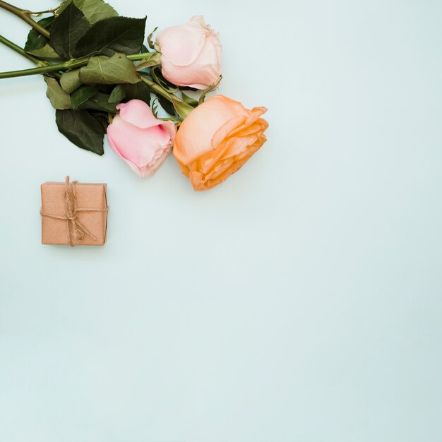 Una vista aérea de tres rosas y una caja de regalo envuelta en un fondo azul pastel