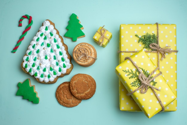 Vista aérea de varias galletas de azúcar de árbol de Navidad y cajas de regalo amarillas sobre fondo azul pastel