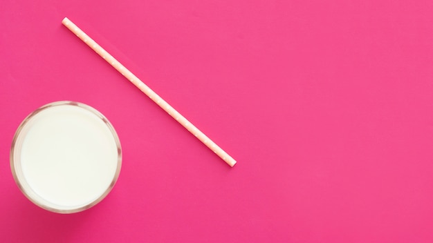 Vista aérea de vaso de leche y paja sobre el fondo rosa