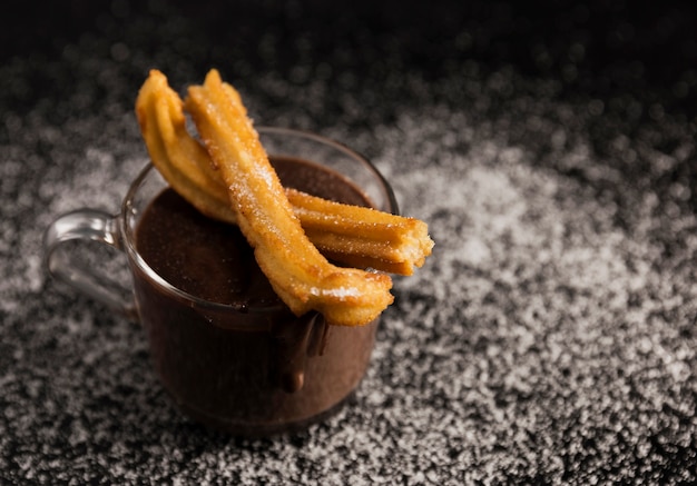 Vista alta de churros encima de la taza con chocolate derretido