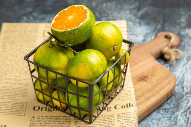 Vista de alta resolución de frutas cítricas frescas en una canasta de periódico sobre tabla de cortar de madera sobre fondo gris