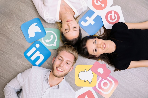 Vista de alto ángulo de amigos acostado en el piso de madera con iconos de redes sociales