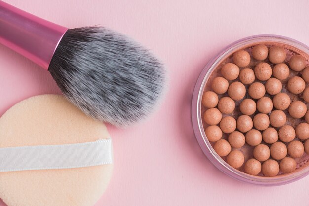 Vista de alto ángulo de bronceado de perlas; cepillo de esponja y maquillaje en superficie rosa