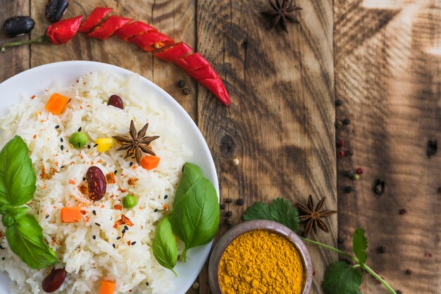 Vista de ángulo alto de arroz vegetal; polvo de cúrcuma; ají rojo y especias secas sobre fondo de madera