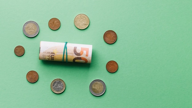 Vista de ángulo alto del billete de banco euro enrollado con monedas sobre fondo verde