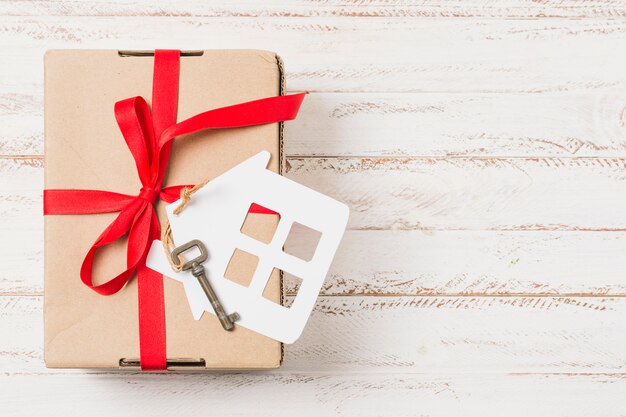 Vista de ángulo alto de una caja de regalo atada con una cinta roja en la llave de la casa sobre una mesa de madera