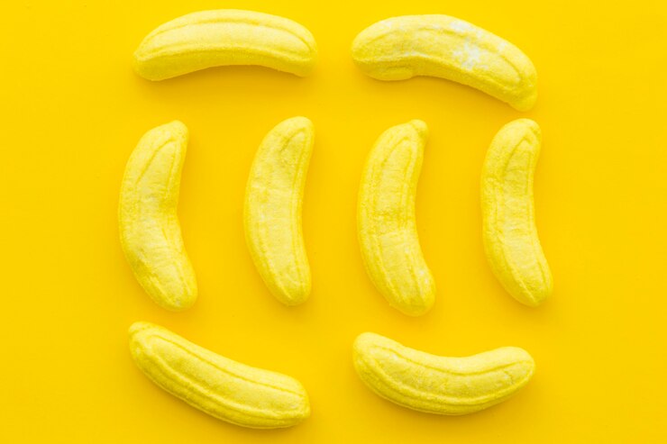 Foto gratuito vista de ángulo alto de caramelos en forma de plátano sobre fondo amarillo