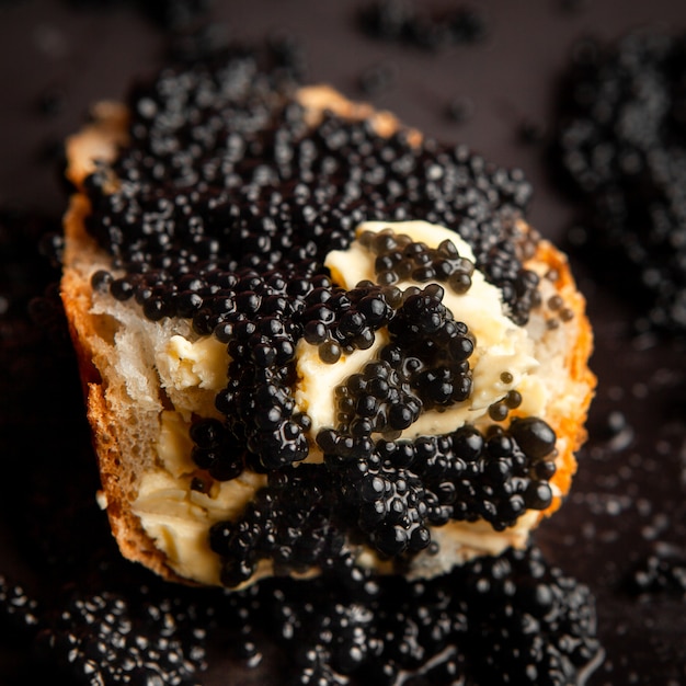 Vista de ángulo alto caviar negro sobre pan sobre fondo oscuro.