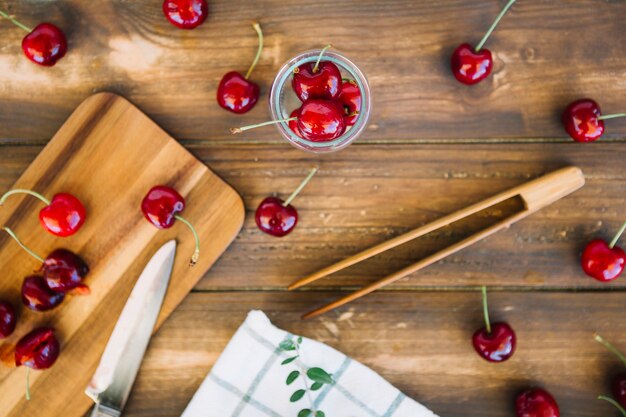 Vista de ángulo alto de cerezas maduras frescas y cuchillo en la tabla de cortar