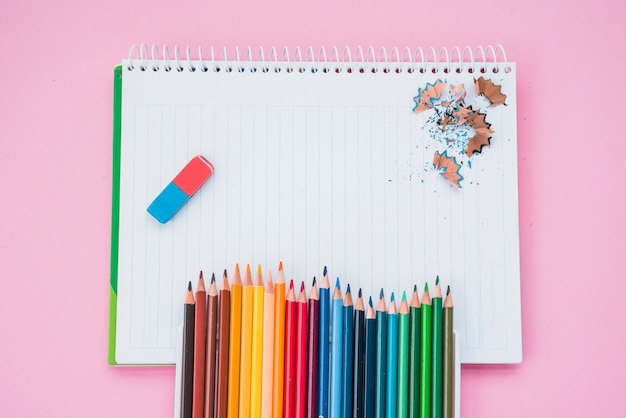 Vista de ángulo alto de los colores de lápiz con borrador y lápiz afeitado en un cuaderno espiral