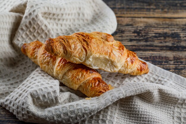 Vista de ángulo alto de croissant en madera y toalla de cocina