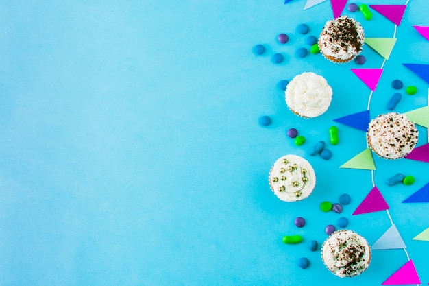 Vista de ángulo alto de cupcakes; caramelos y empavesado sobre fondo azul