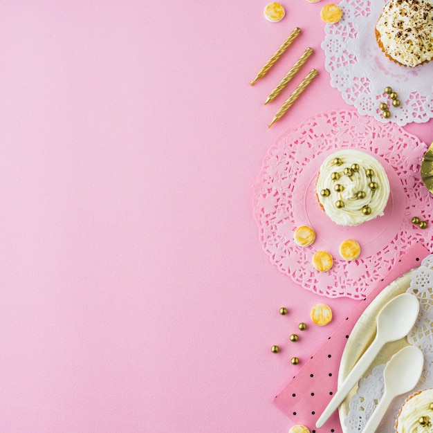 Vista de ángulo alto de cupcakes; dulces y velas sobre fondo rosa