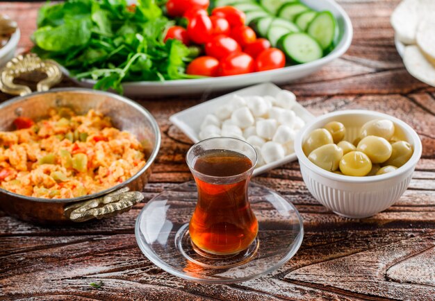 Vista de ángulo alto deliciosa comida en plato con una taza de té, ensalada, encurtidos en superficie de madera