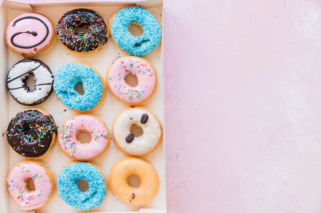 Vista de ángulo alto de deliciosos donuts en caja en superficie rosa
