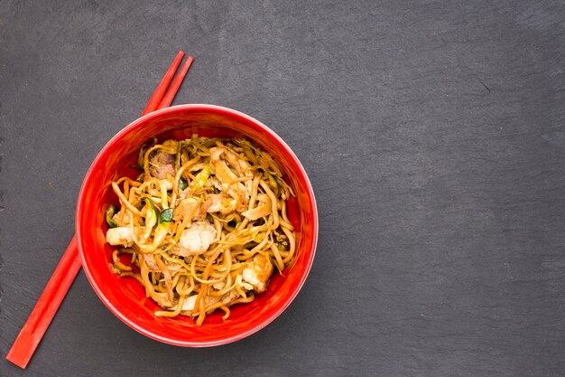 Vista de ángulo alto de deliciosos fideos chinos en un tazón con palillos sobre una superficie negra