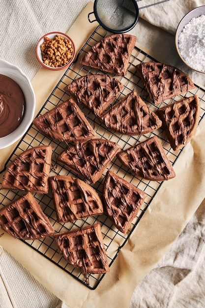 Vista de ángulo alto de deliciosos gofres de chocolate en una red sobre la mesa cerca de los ingredientes