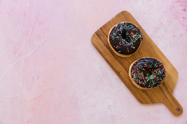 Vista de ángulo alto de donuts de chocolate fresco en tabla de cortar de madera