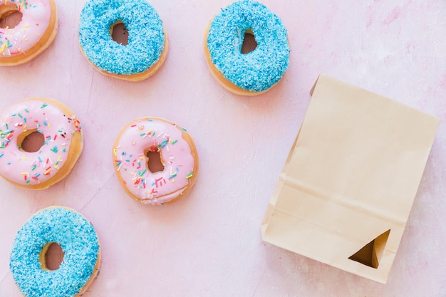 Vista de ángulo alto de donuts frescos y paquete sobre fondo rosa