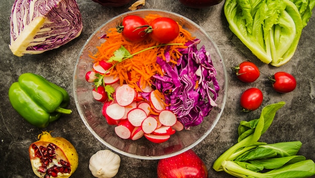Vista de ángulo alto de ensalada fresca en un recipiente de vidrio rodeado de verduras y frutas