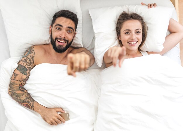 Vista de ángulo alto de la feliz pareja acostado en la cama señalando los dedos