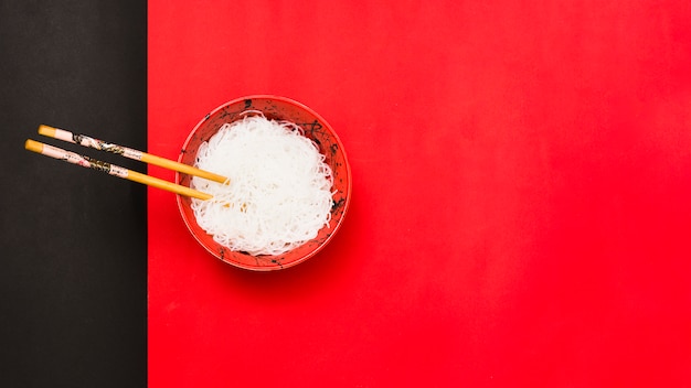 Foto gratuita vista de ángulo alto de fideos blancos en un tazón con palillos sobre doble fondo