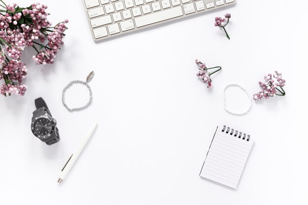 Vista de ángulo alto de la flor; pulsera; reloj de pulsera; bolígrafo; bloc de notas espiral y teclado sobre fondo blanco