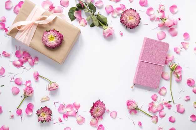 Vista de ángulo alto de flores; Caja de regalo y diario sobre superficie blanca.