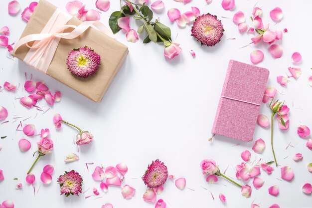 Vista de ángulo alto de flores; Caja de regalo y diario sobre superficie blanca.