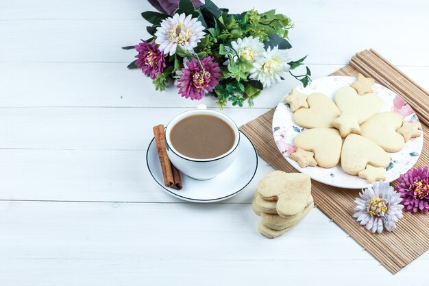 Vista de ángulo alto galletas en forma de corazón y estrella, flores en mantel con taza de café