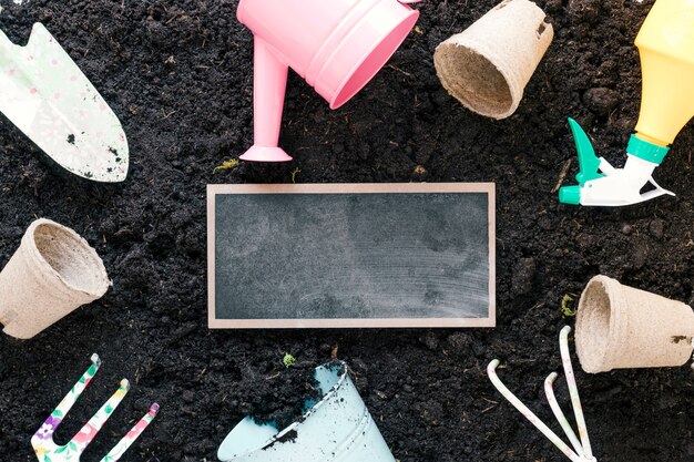 Vista de ángulo alto de herramientas de jardinería y pizarra en blanco sobre la suciedad negra