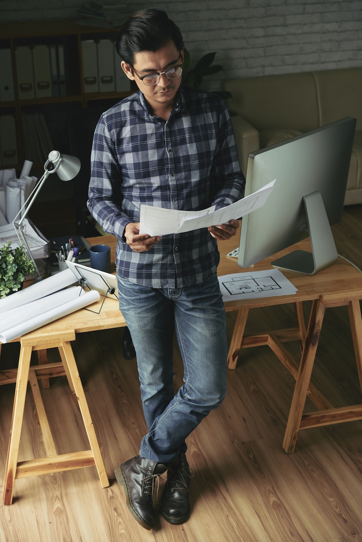Foto gratuito vista de ángulo alto del hombre asiático de pie en la mesa examinando planos