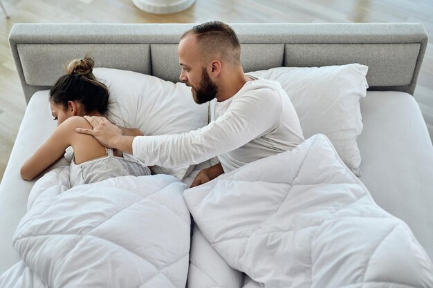 Vista de ángulo alto de un hombre tratando de hablar con su novia disgustada que lo ignora en el dormitorio